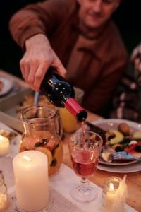 Faceless man pouring rose wine while having dinner with candles in garden in twilight